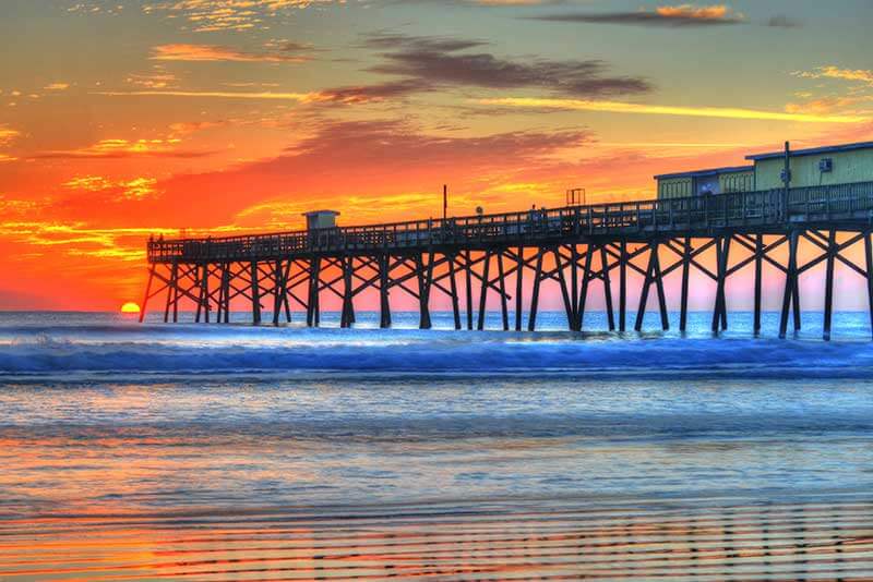 An orange sunset and a long wooden pier in Daytona Beach, Florida