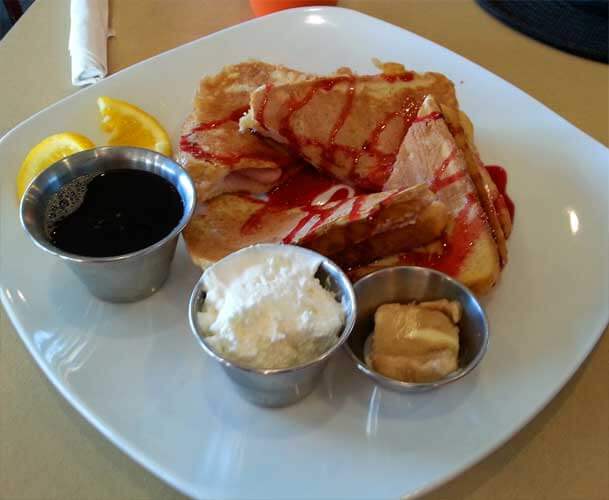 A white plate of French toast with metal cups for syrup, whipped cream and butter in Indiana Dunes, Indiana