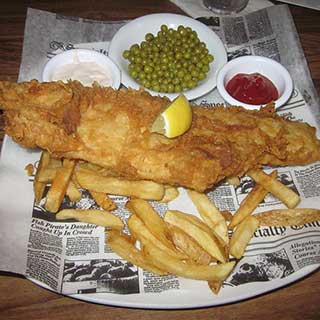 A slice of fried fish, fries and round white bowls of mayonnaise, green peas and ketchup served on newspaper at Fionn McCool’s Irish Pub in Jacksonville, Florida