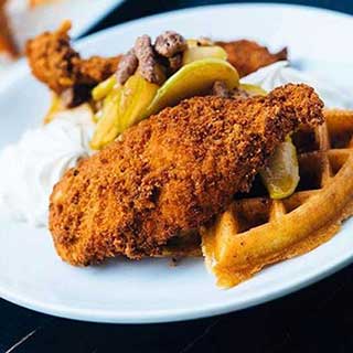 A round white plate displays fried chicken and waffles with sliced cooked apples at Candy Apple Cafe in Jacksonville, Florida