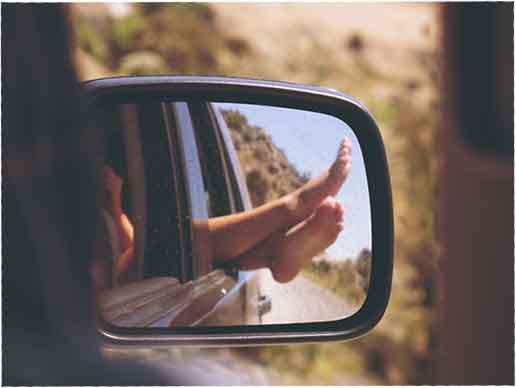 A rearview mirror reflects feet dangling outside the car window in Jacksonville, Florida