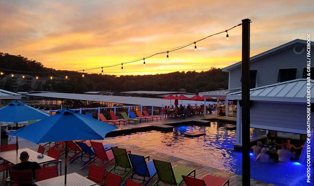 A lakeside pool surrounded by deck chairs, shown in front of a yellow sunset at Boathouse Lakeside Bar & Grill in Lake of the Ozarks, MO