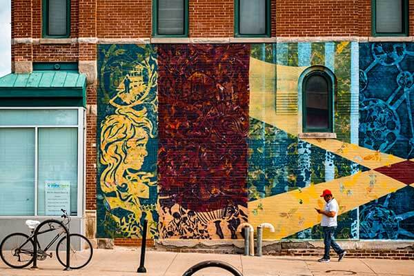 A man with a red hat walks in front of the Magic City mural in Omaha, Nebraska