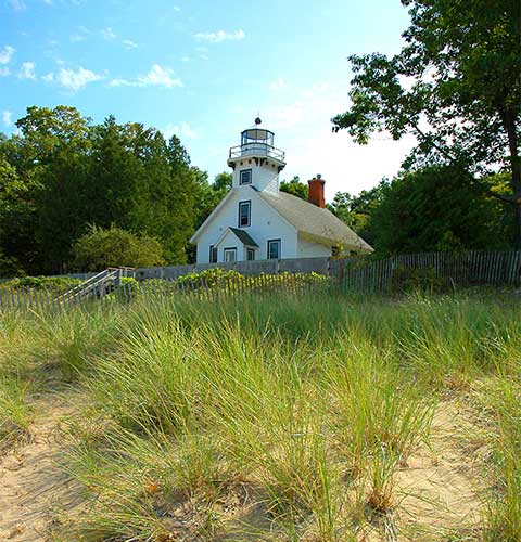 Mission Point Lighthouse stands surrounded by green grass and tall trees in Traverse City, Michigan