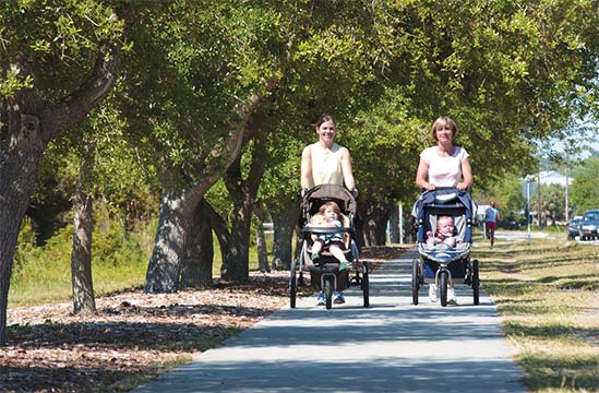 Two women push strollers with young children and walk along a path on The Loop in Wrightsville Beach, North Carolina
