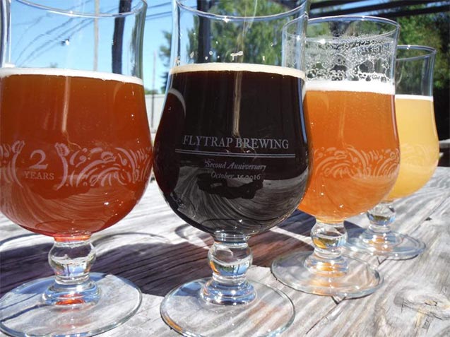 Four beers in curved glasses sit on a wooden table at Flytrap Brewing in Wilmington, North Carolina