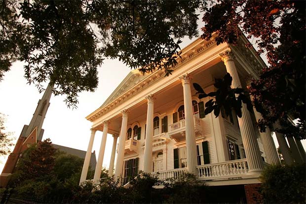 The Bellamy Mansion Museum has tall white columns and is surrounded by green trees in Wilmington, North Carolina