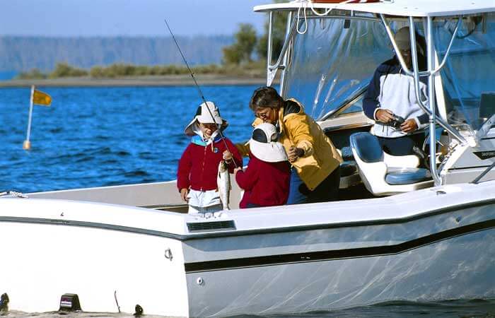 A woman teaches two kids to fish on a white boat on Lake Yellowstone at Yellowstone National Park in Wyoming