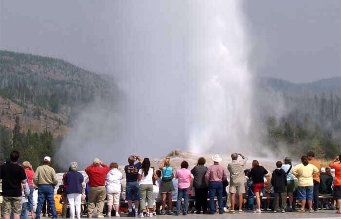 A crowd of people watch an eruption of Old Faithful at Yellowstone National Park in Wyoming
