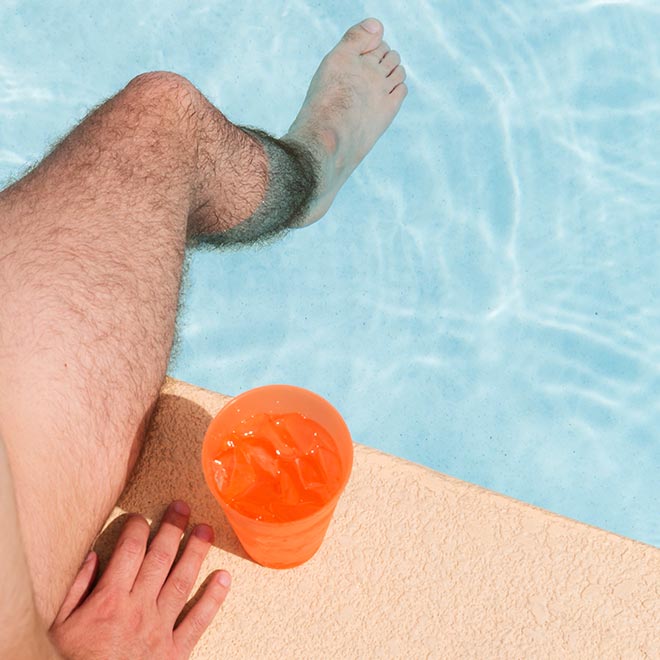 Man's leg and an iced beverage by the pool