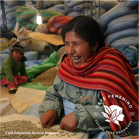 A smiling woman involved in the Café Femenino Bolivia Program wears a red scarf while touching coffee beans