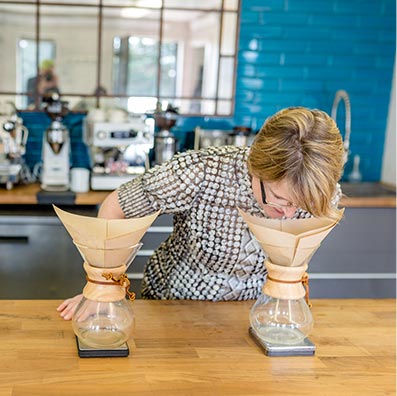 A woman wearing glasses smells roasted coffee beans produced by Café Femenino at Snake River Roasting Co. in Jackson, WY