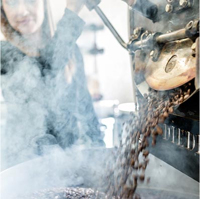 Freshly roasted Café Femenino coffee beans surrounded by steam fall out of a roasting machine at Snake River Roasting Co. in Jackson, Wyoming