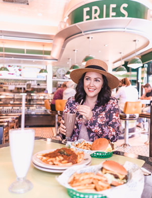 Influencer Ashley Buchanan holds a chocolate milkshake, sitting at a table with hamburgers at Goody Goody in Tampa Bay, Florida