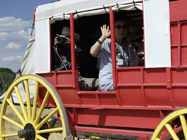 A woman waves from a red stagecoach with yellow wheels in Albany County, Wyoming