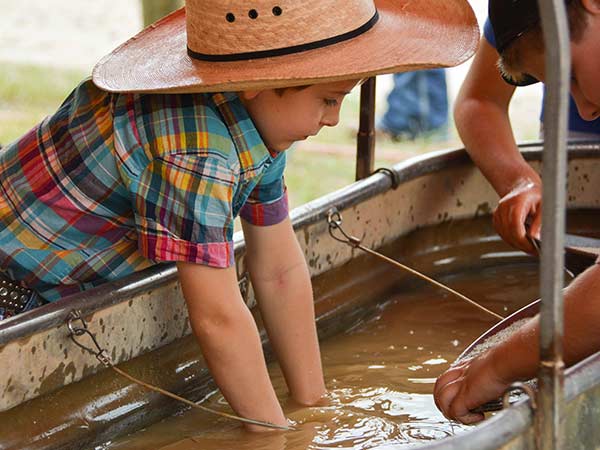 A child wearing a cowboy hat puts his hands in a tub of water while panning for gold in Old Frontier Town at the Cheyenne Frontier Days Rodeo in Cheyenne, Wyoming