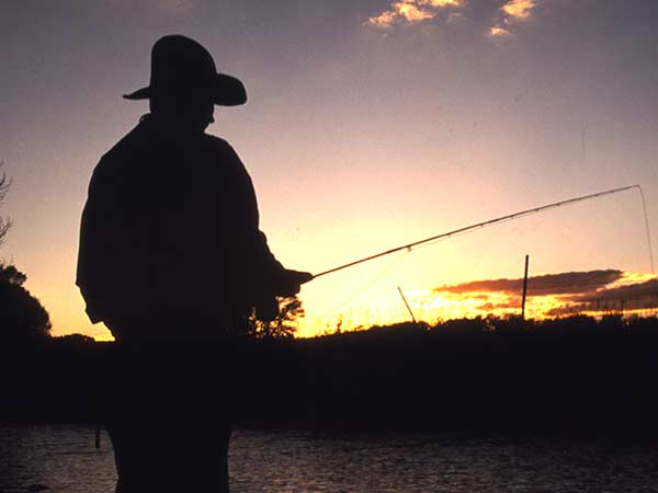 The silhouette of a man wearing a cowboy hat and fishing during sunset at a dude ranch in WY