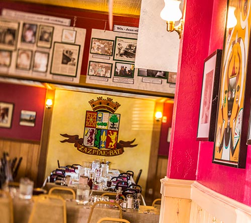 Inside the J.T. Basque Bar & Dining Room with a zazpiak-bat sign on the wall in the back and tables set with dinnerware in the foreground. 