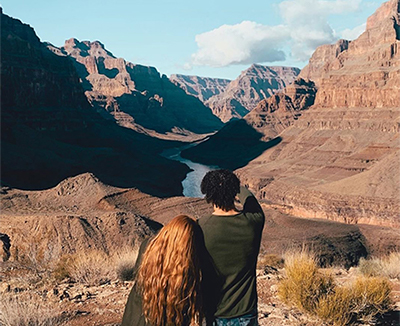 A photograph shows a man and a woman from behind as they look over the Grand Canyon