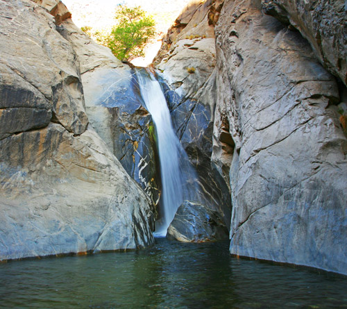 A waterfall flowing over a gray rock face into a natural turquoise pool in Tahquitz Canyon in Palm Springs, California