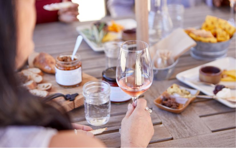A young woman holds a glass of crisp rosé at a table of small bites and appetizers