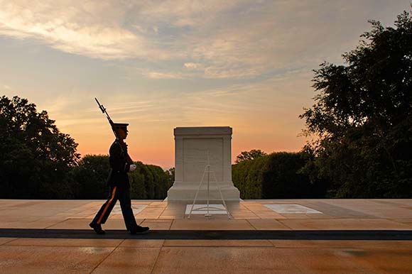 A soldier in full military uniform marches in front of the Tomb of the Unknown Soldier carrying his M-14 rifle at sunset in Arlington National Cemetery