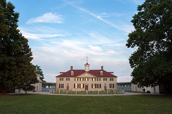 George Washington’s Mount Vernon Estate flanked by two massive trees on green grounds.