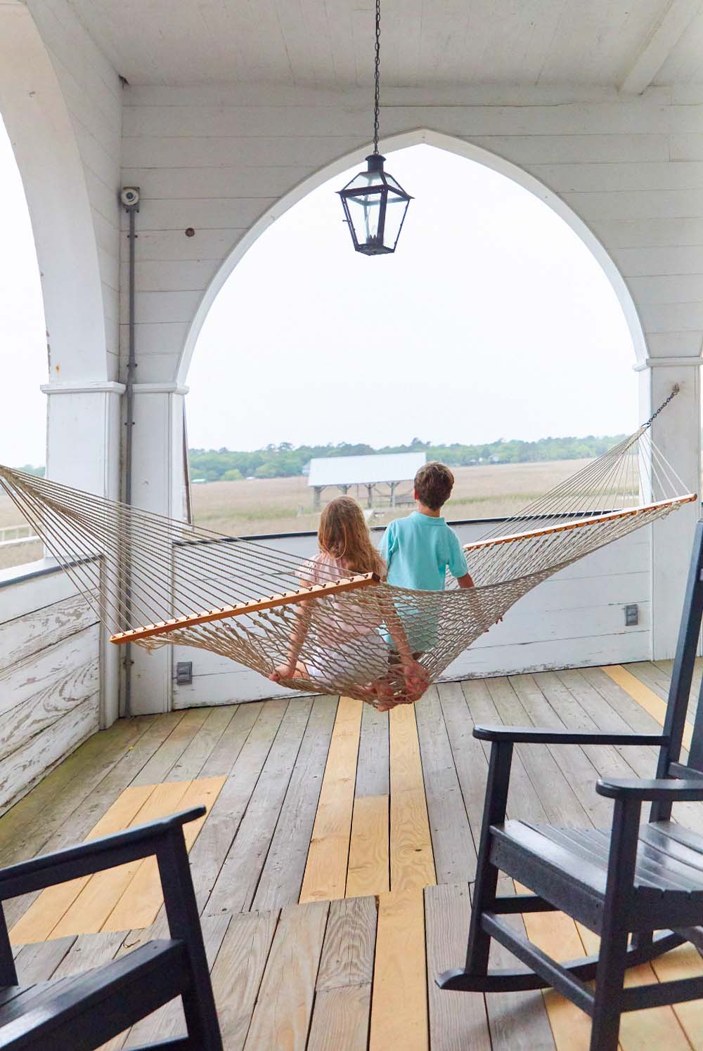 A young boy and girl sit together in a hammock on the Pelican Inn’s porch overlooking the marshwaters on Pawleys Island, South Carolina.