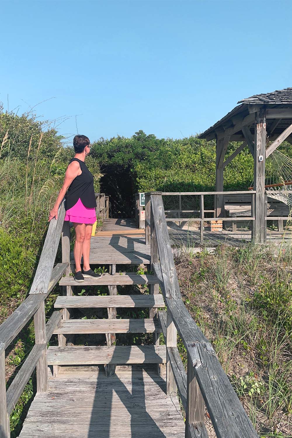 A woman in summer clothes standing on the steps that lead to the beach from the Pelican Inn on Pawleys Island, South Carolina.