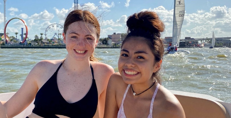 Two friends pose on the deck of a boat with the rides of Kemah Boardwalk in the background in Bay Area Houston