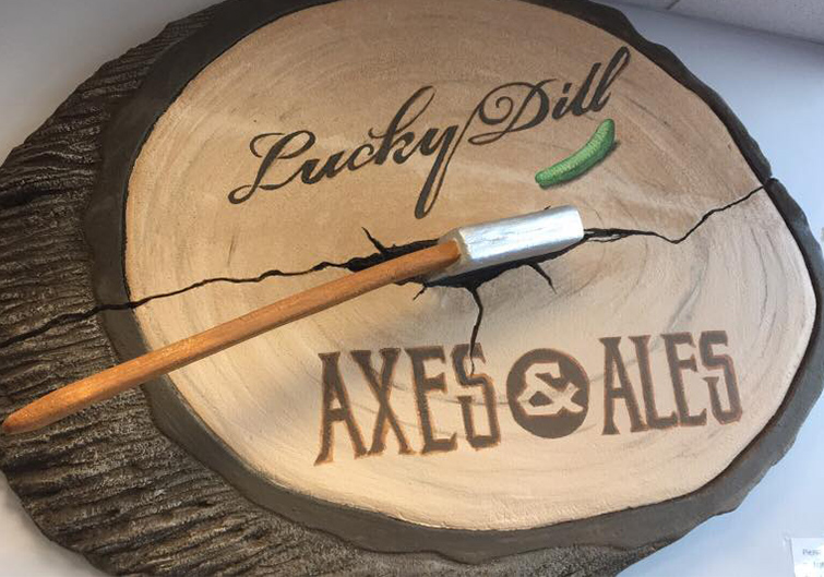 AA storefront sign that looks like a slice from a wooden log reads “Lucky Dill, Axes & Ales” in burnt script in Charleston, West Virginia.