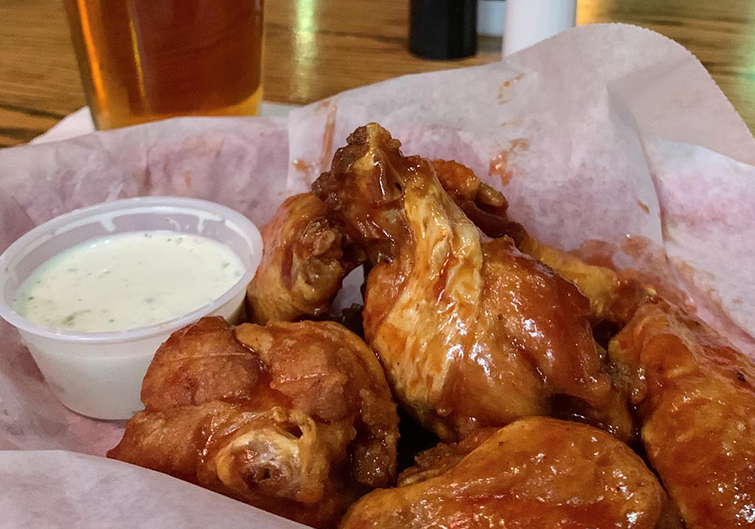 A basket of friend chicken wings are drizzled in sauce with a side of Ranch dressing next to them. 