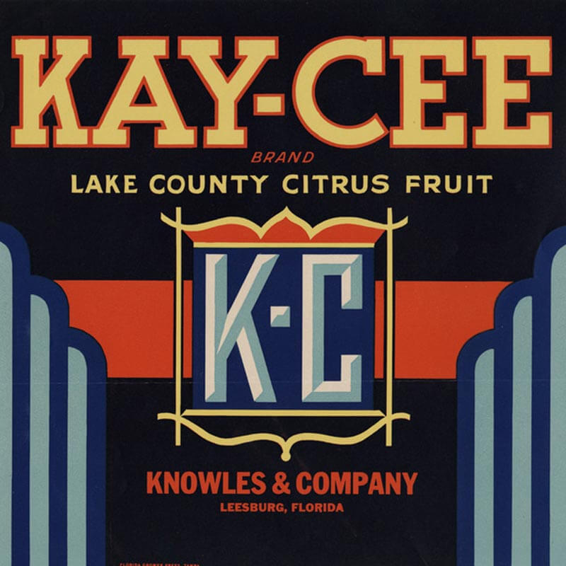 An illustrated Kay Cee brand citrus label is blick, with blue edging, yellow letters and a large, blue K C in the middle of a thin yellow square.