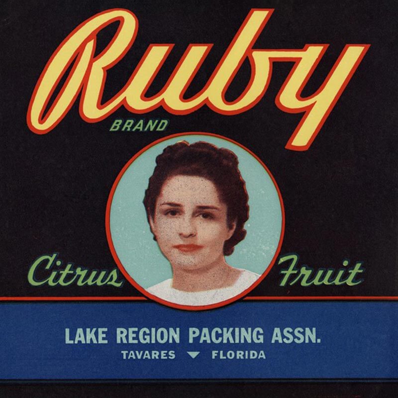 A Ruby brand citrus label has a photograph of a woman with brunette hair in the middle of a black square. Red and yellow letters are across the top.