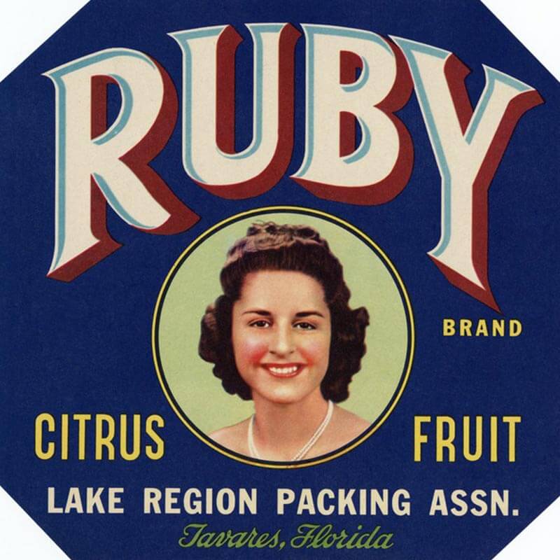A Ruby brand citrus label has a photograph of a woman with brunette hair in the middle of a blue circle. Red and cream letters are across the top.