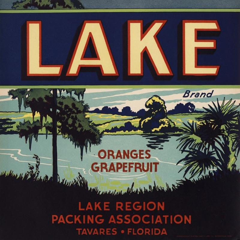 An illustrated Lake brand citrus label shows a lake with surrounding greenery, yellow and red letters and a blue background.