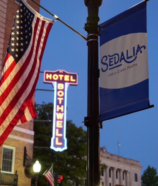 Sedalia, MO light pole with Sedalia flag and the American flag, with Hotel Bothwell signage in the background