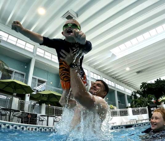 Man in pool holds up a splashing little boy at Oasis Hotel in Springfield, Missouri