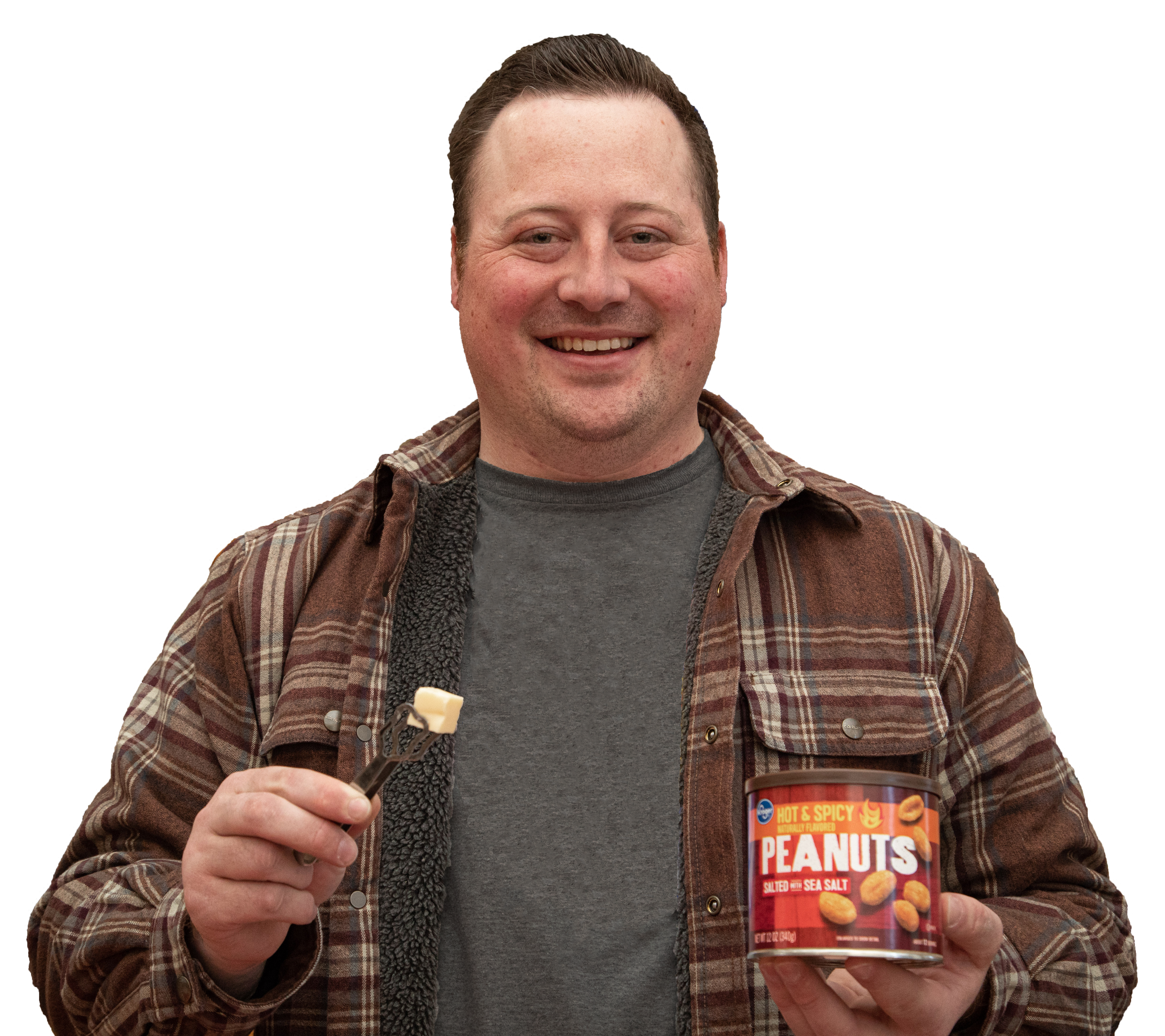 A man wearing a grey t-shirt and a brown flannel jacket holds a cube of cheese using small silver tongs in one hand and a can of peanuts in the other hand.