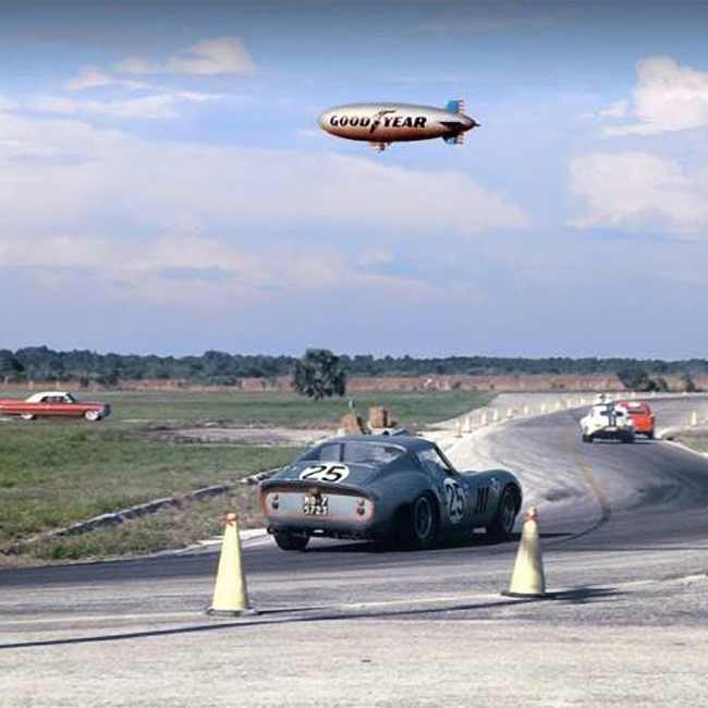 A silver GoodYear blimp hang overhead as a blue, vintage-style, number 25 car turns a corner at the Sebring International Raceway in Sebring, Florida.