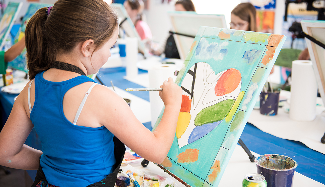 A young girl in a blue tank top paints a canvas with a colorful  heart at the Highlands Arts League in Sebring, Florida.