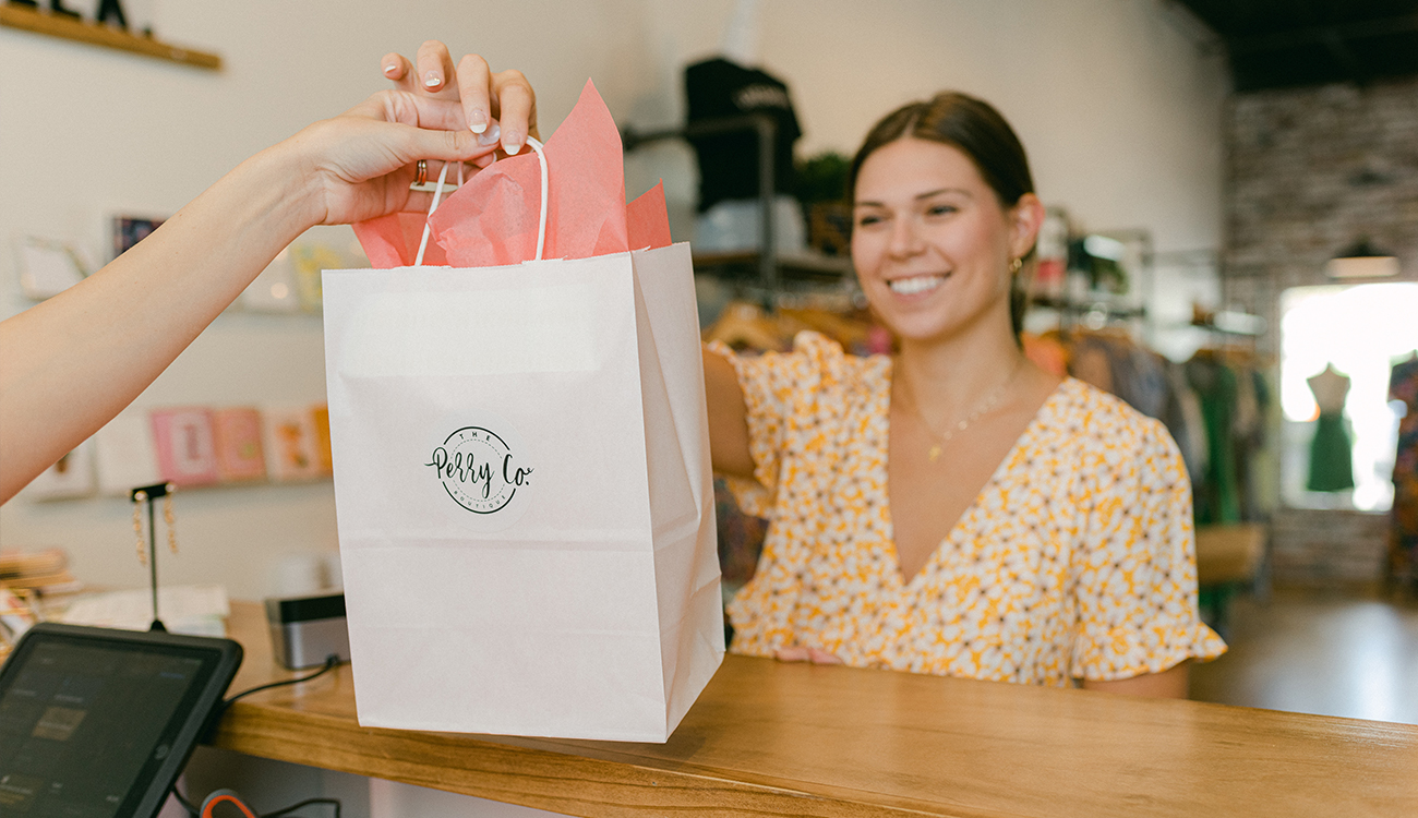 A female customer smiles as she receives a bagged, purchased item over the counter at The Perry Co. Boutique in Lake Placid, Florida.