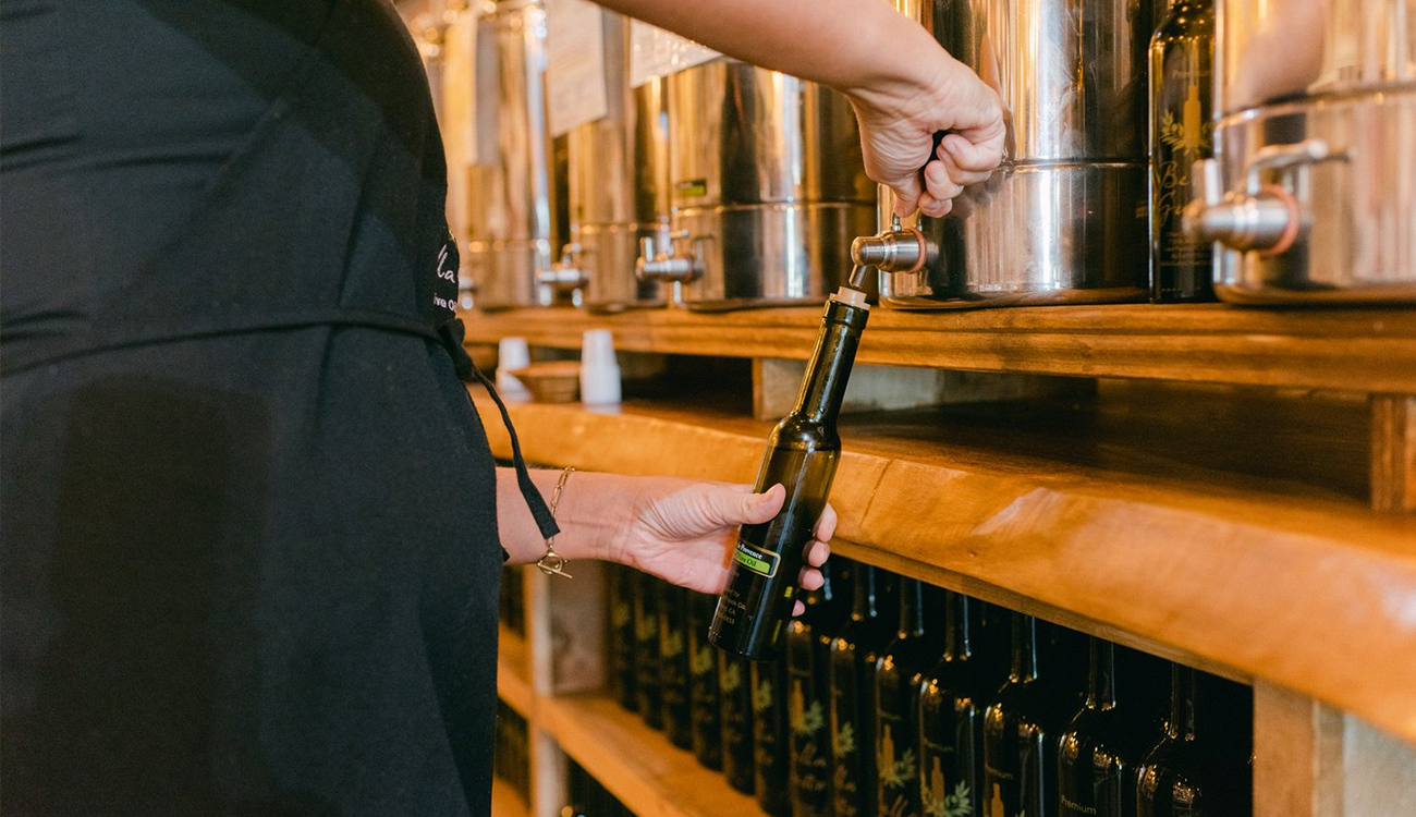 A female worker in a black apron pours olive oil into a brown glass bottle to sell at Bella Gusto Olive Oil Co. in Lake Placid, Florida. 