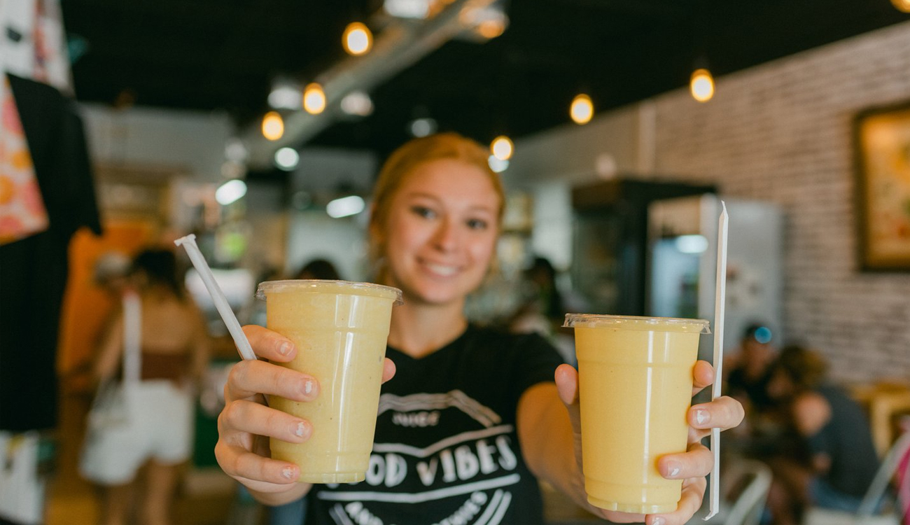 A young female worker holds out two drinks ready to be enjoyed at Good Vibes Juice and Smoothies in Lake Placid, Florida.