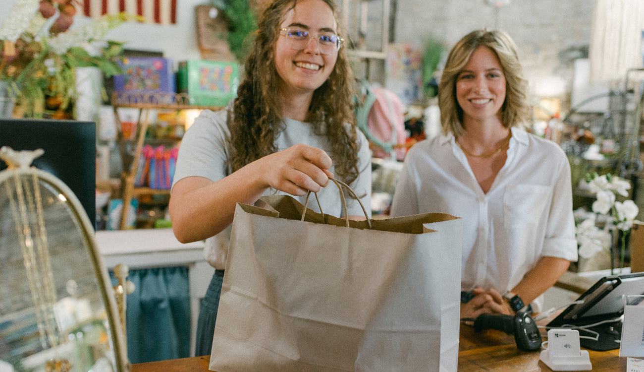 Two females stand smiling behind the register with a brown bag of purchased items at The Blueberry Patch in Lake Placid, Florida.
