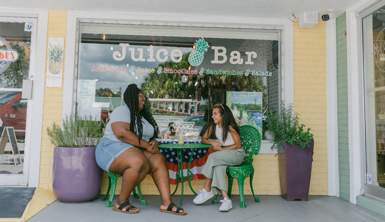 A Black woman and young gifrl sit at a green patio table enjoying smoothies from Good Vibes Juice and Smoothies in Lake Placid, Florida.