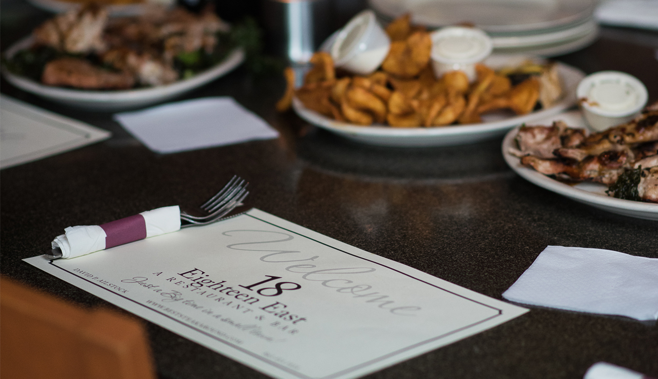 A paper placement with the restaurant logo and several platters of food rest on a table at Eighteen East Restaurant & Bar in Avon Park, Florida.